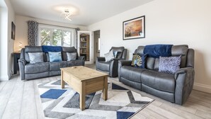 A modern living room with two leather sofas, a wooden coffee table, and a patterned rug. - Martello View - 3 Bedroom - Llanreath (Pembroke Dock)