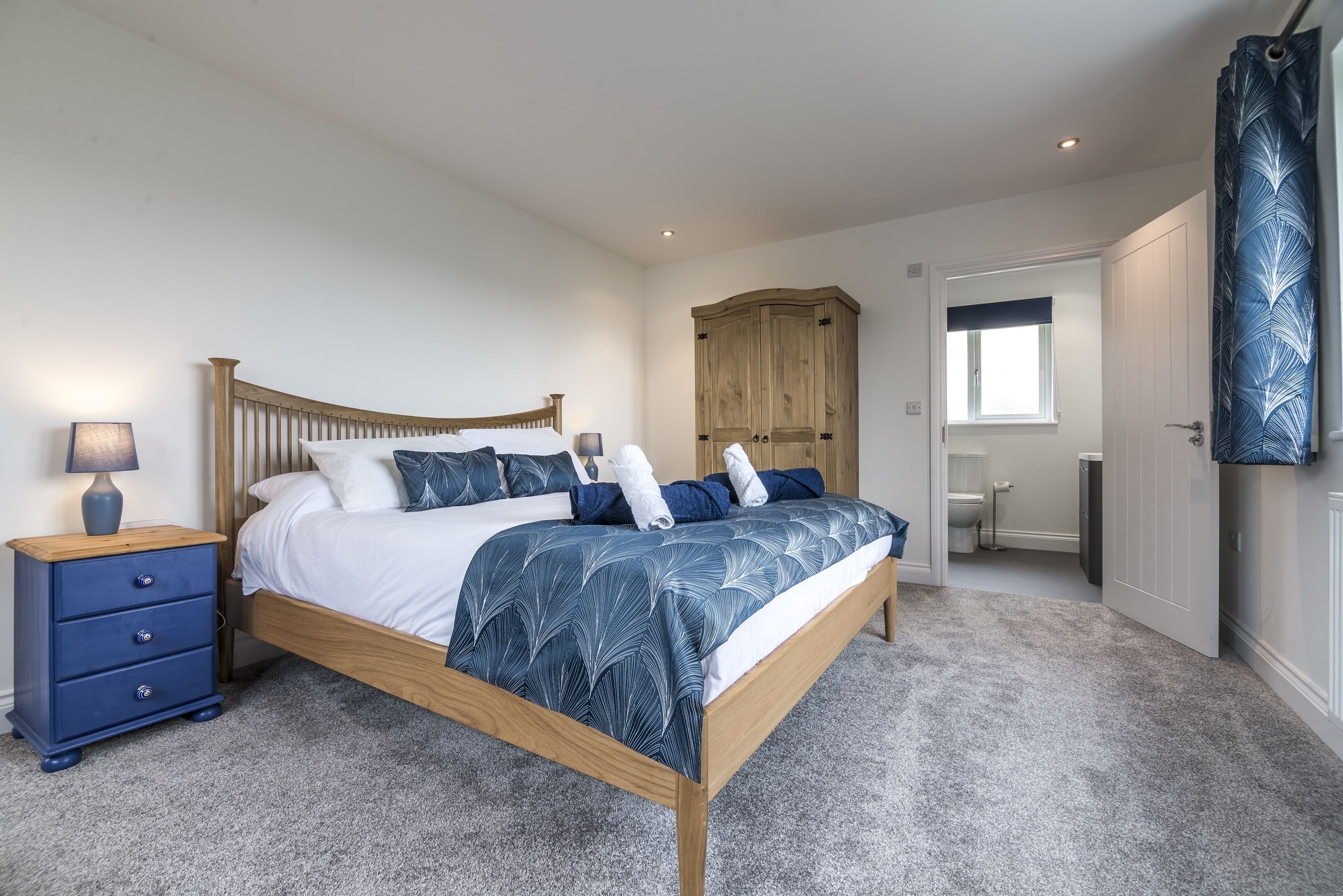 A bedroom with a wooden bed, a nightstand, a wardrobe, and a bathroom visible through an open door.