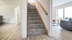 A staircase with carpeted steps and wooden handrails, leading to a room with a view. - Martello View - 3 Bedroom - Llanreath (Pembroke Dock)