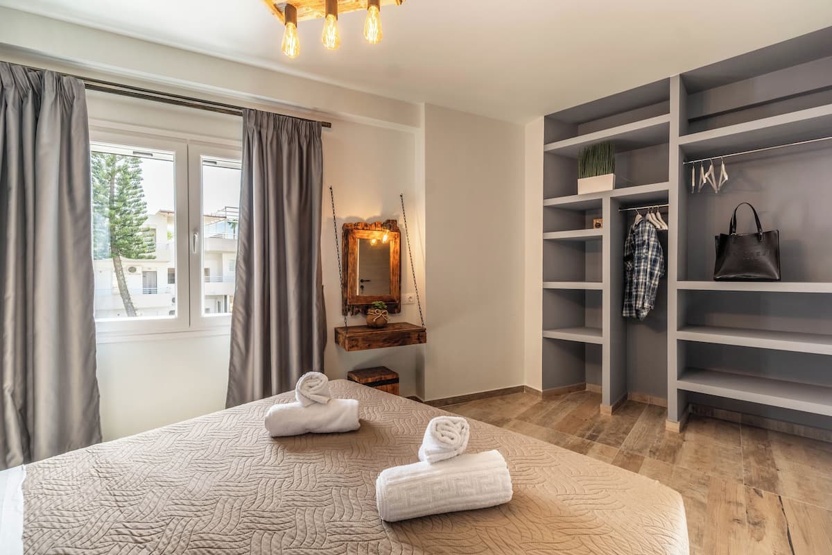 A bedroom with a bed, a mirror, a wardrobe, and a window with curtains.