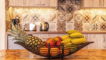 Una mesa de madera con un frutero que contiene piña, mango y plátanos.