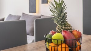 Una mesa de comedor con una cesta de frutas que contiene una piña, mango, manzana y naranjas.