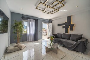 Una sala de estar moderna con una mesa de centro de vidrio, un sofá gris y un gran ventanal con cortinas.