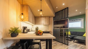 Una cocina moderna con armarios de madera, una isla central con taburetes y una zona de comedor con sofá negro y cojines amarillos.