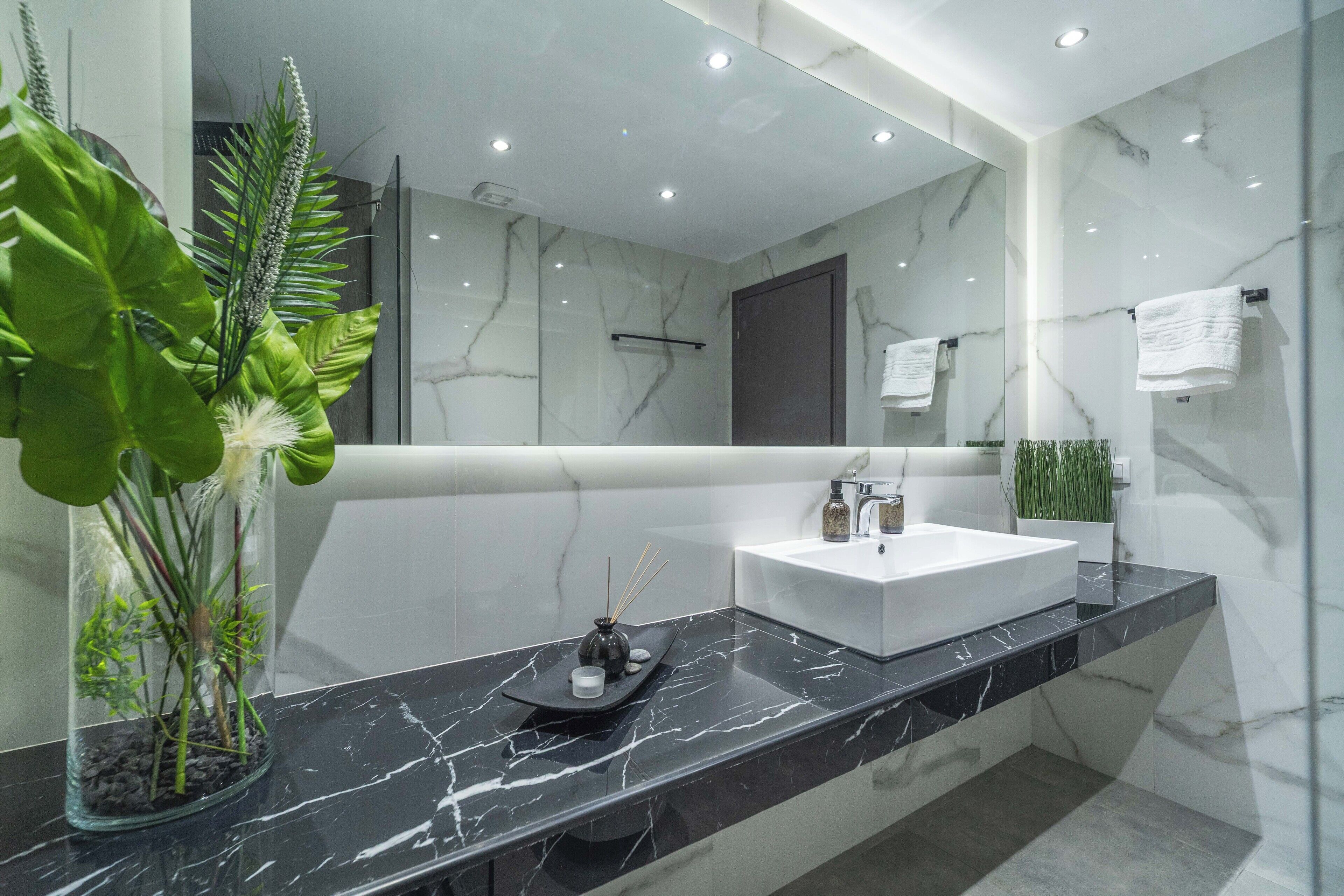 Une salle de bain moderne avec un grand miroir, un lavabo blanc et un plan de toilette en marbre noir.