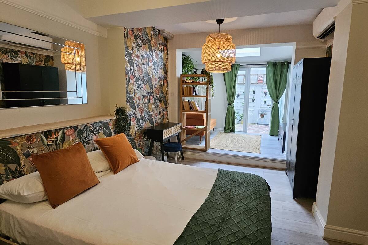 A bedroom with a bed, a TV, a bookshelf, and a view of the outside.