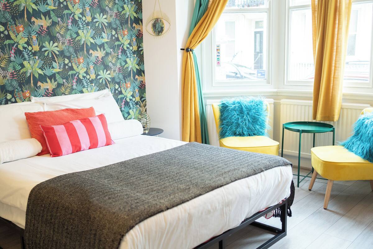 A bedroom with a bed, pillows, a window with curtains, a small round table, and two chairs.
