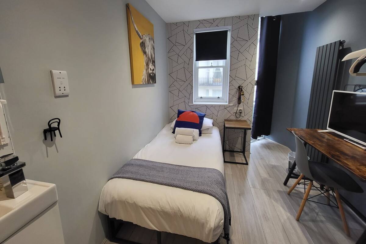 A modern bedroom with a bed, a desk, a chair, and a TV.