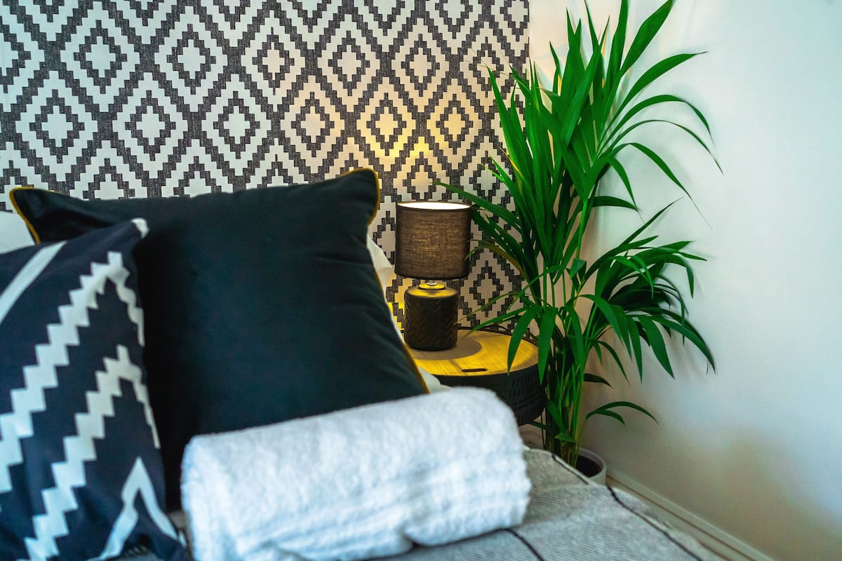 A bed with black and white patterned pillows, a lamp, and a potted plant.