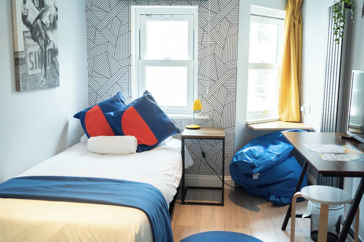 A bedroom with two beds, a desk, a chair, and a window with curtains.