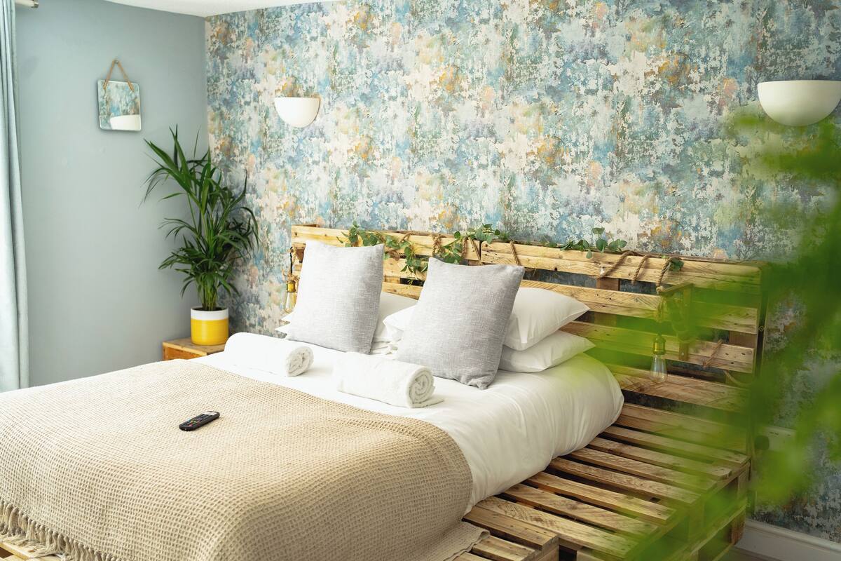 A bedroom with a wooden bed, white bedding, a small bedside table with a lamp, and a potted plant.