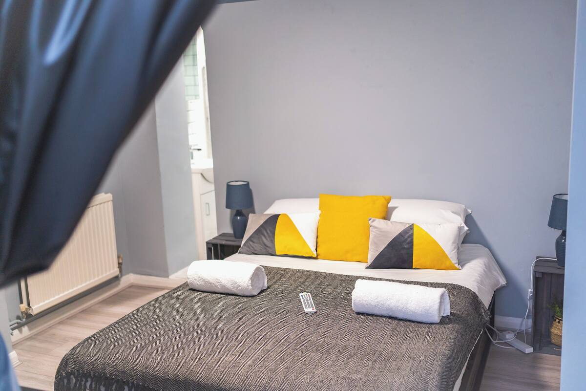 A hotel room with a bed, a nightstand, a lamp, and a view of the outside.