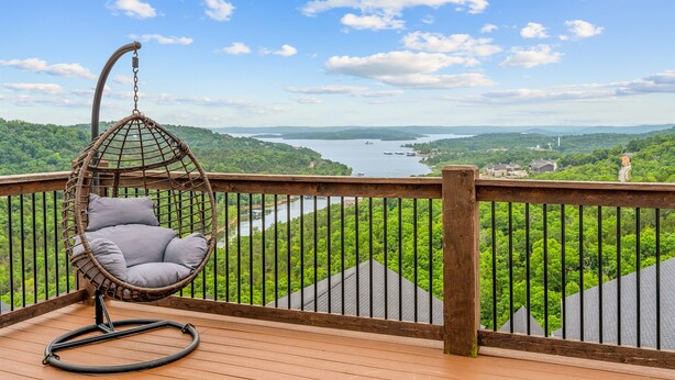 A wooden deck with a hanging chair overlooking a river and forested landscape. - Beautiful Lake Views, Indoor and Outdoor Pool, Private Hot Tub, and Game Room! (Branson)