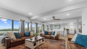 A spacious living area with a large window, a ceiling fan, and a kitchen in the background. - Beautiful Lake Views, Indoor and Outdoor Pool, Private Hot Tub, and Game Room! (Branson)
