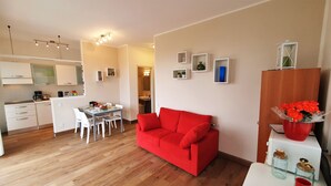 Un espace de vie compact comprenant un coin repas, une kitchenette et un canapé rouge.