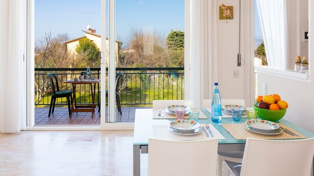 Un coin repas avec une table dressée pour deux personnes, une vue sur l’extérieur et un balcon avec des chaises.