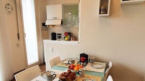 Un coin repas avec une table dressée pour deux personnes, agrémentée d’un saladier de fruits, d’un croissant et de deux tasses.