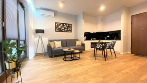 Ein modernes Wohnzimmer mit einem grauen Sofa, zwei kleinen runden Tischen und einem Essbereich mit einem schwarzen Stuhl.