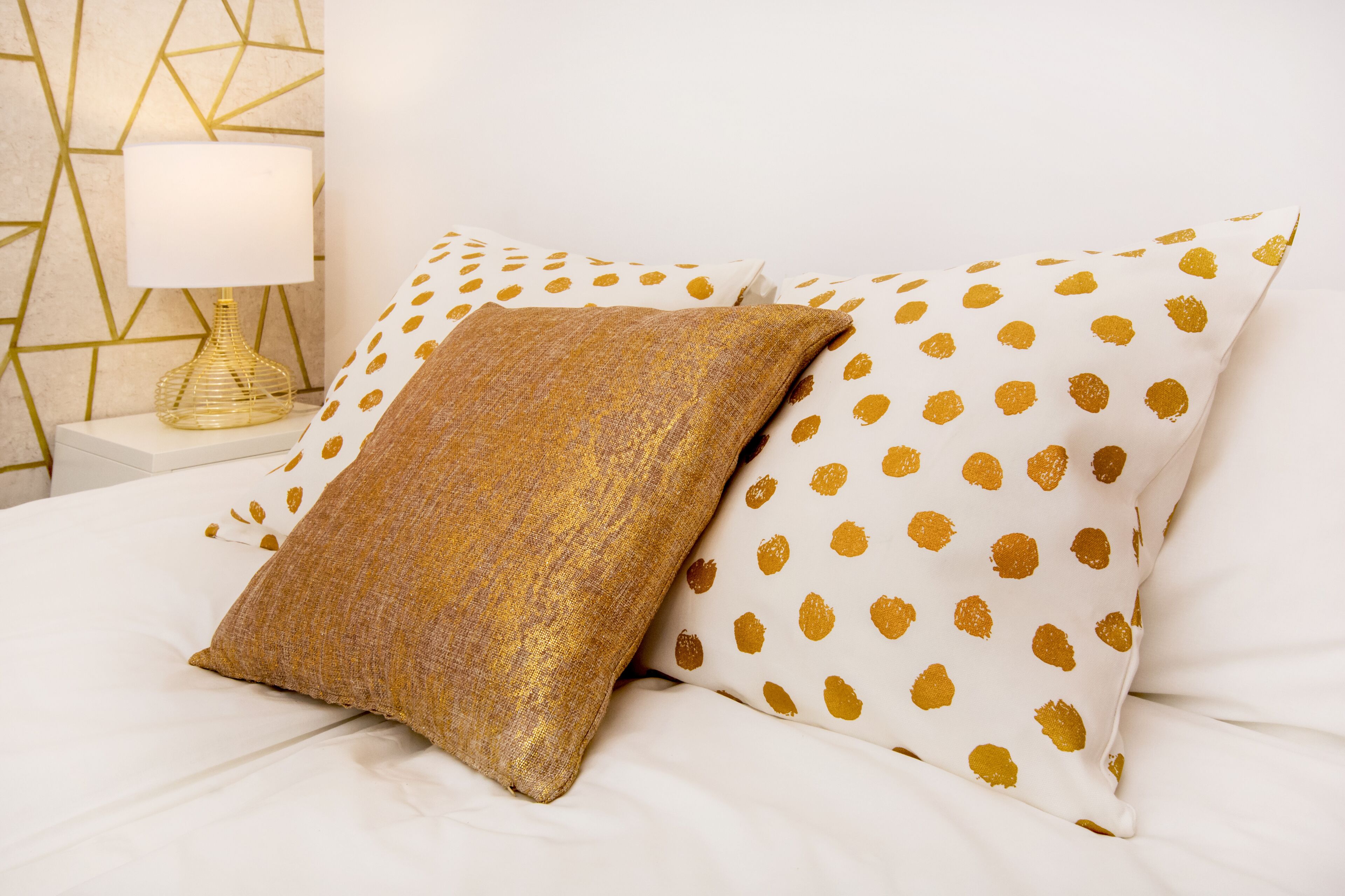 A bed with white bedding and two pillows, one with a gold pattern and the other with a gold and brown pattern.