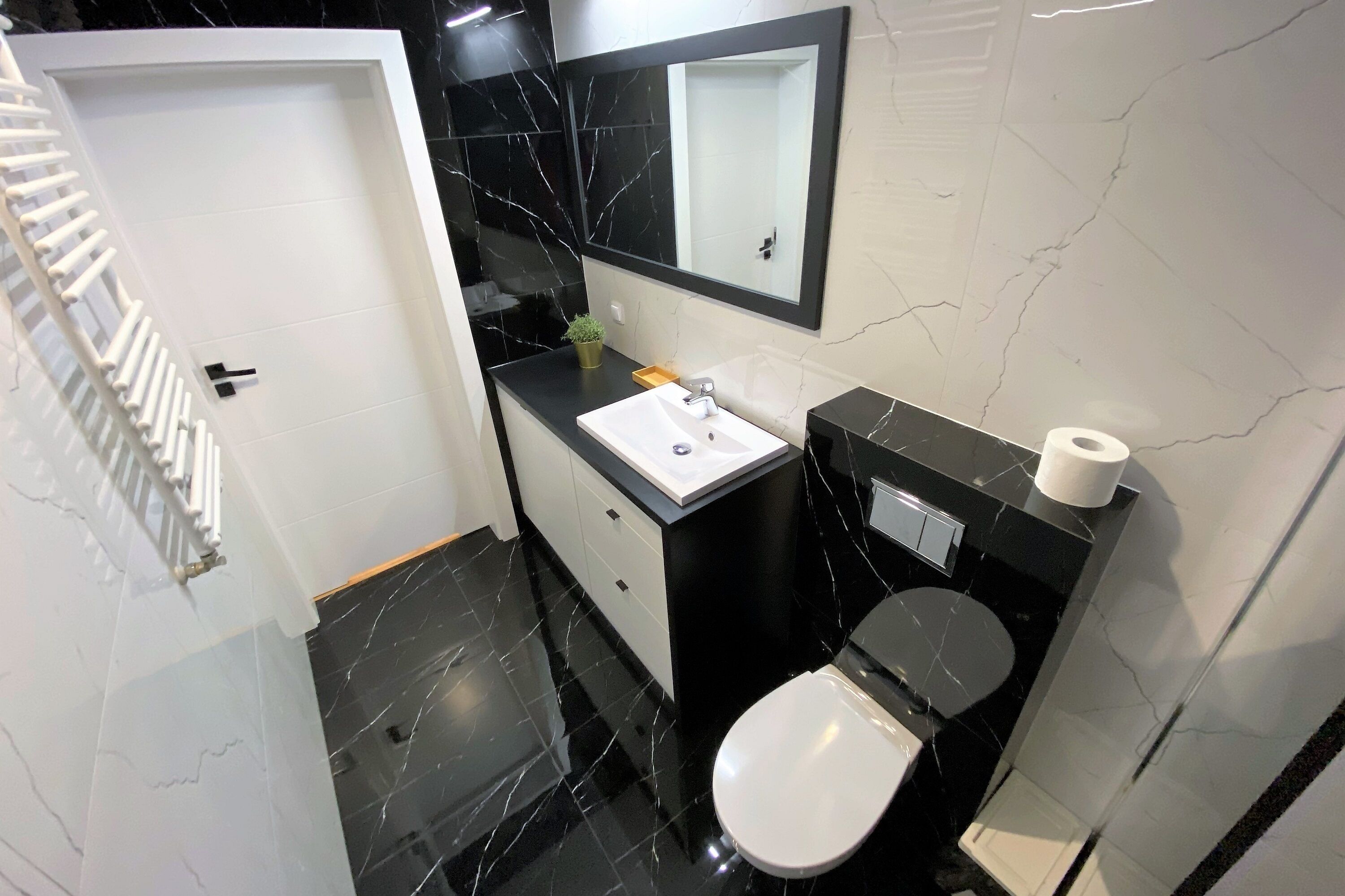 Un baño moderno con lavamanos blanco, salpicadero de mármol negro y un inodoro.