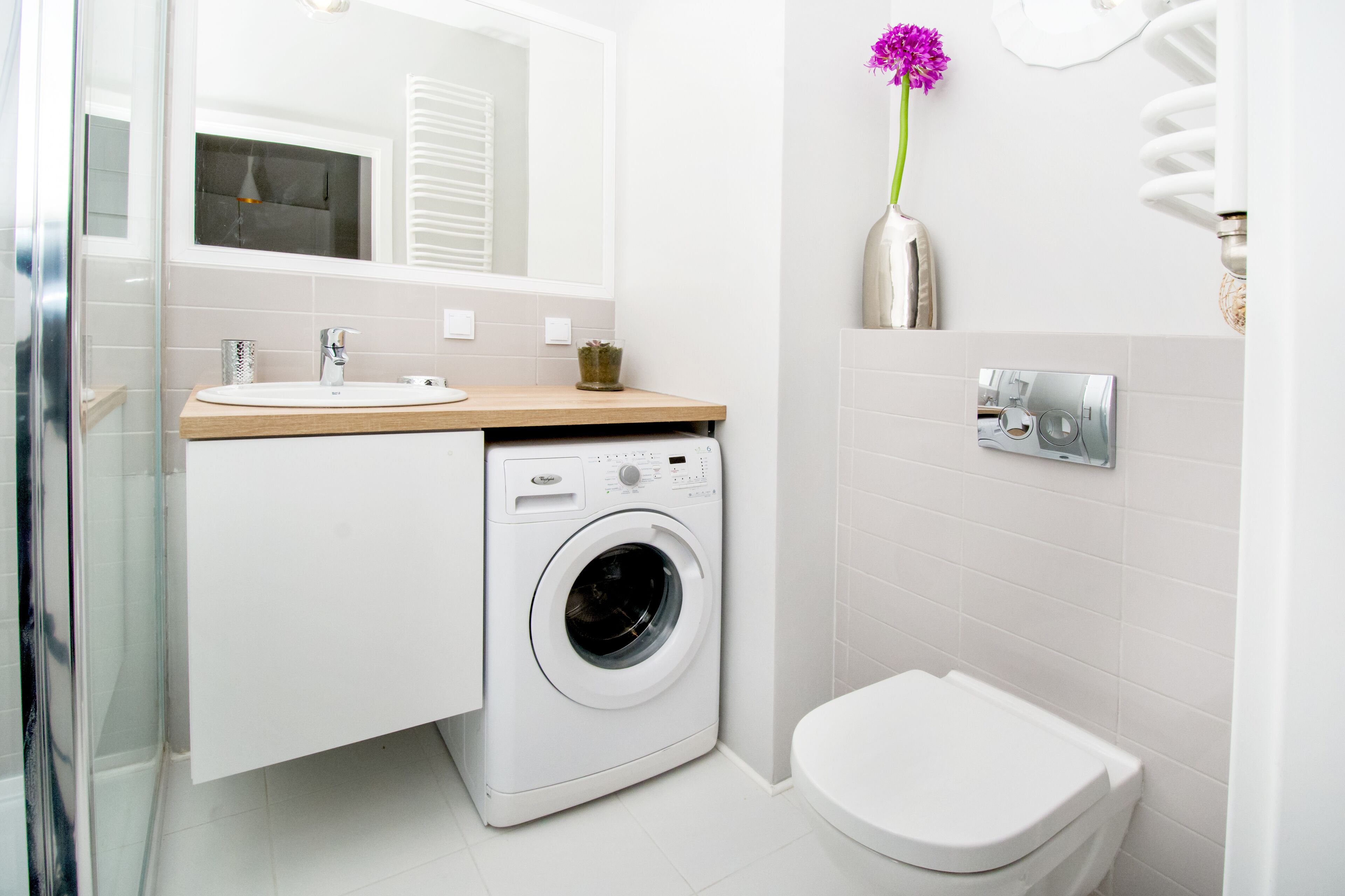 A modern bathroom with a built-in washing machine, a toilet, and a sink with a wooden countertop.