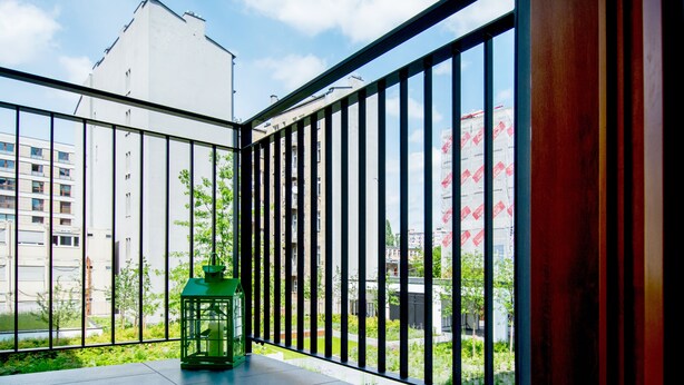 Ein Balkon mit einer grünen Laterne, Metallgeländern und Blick auf Gebäude und Grünflächen.