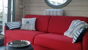 Ein rotes Sofa mit gestreiften Kissen, eine Metallschale und ein runder Spiegel an der Wand.