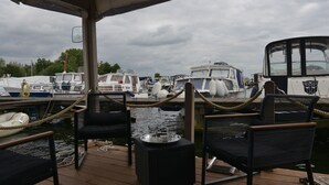 Eine überdachte Terrasse mit vier schwarzen Stühlen und einem kleinen Tisch, mit Blick auf einen Yachthafen mit verschiedenen Booten.