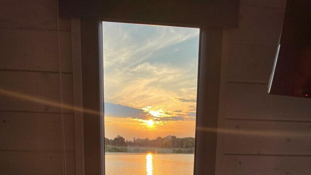 Ein Sonnenuntergang über stillen Gewässern, betrachtet durch ein Fenster mit Holzwänden.
