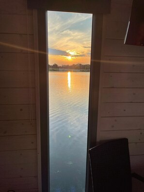 Vista del atardecer sobre un cuerpo de agua tranquilo desde una ventana con paredes de madera.