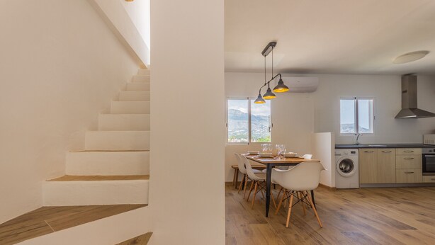Una cucina moderna con pavimento in legno, un'area pranzo con tavolo e sedie e una scala con pareti bianche.