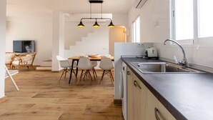 Una cucina moderna con pavimento in legno, zona pranzo con sedie, lavandino e una scala che conduce a un altro livello.