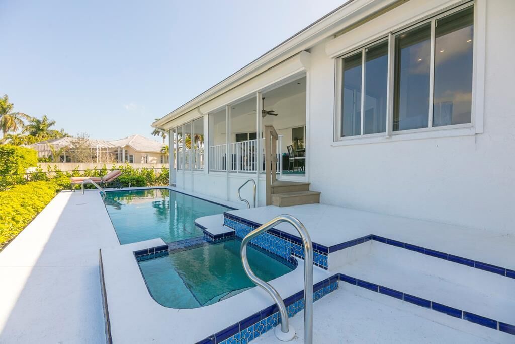 A swimming pool with a covered patio area, a clear sky, and a view of neighboring houses.