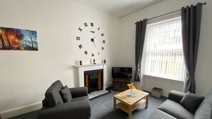 A living room with a fireplace, a large wall clock, and a sofa.