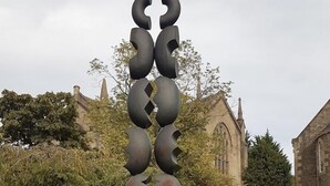 A sculpture in a grassy area with a church in the background.