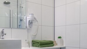 A modern bathroom with a white sink, green towels, a small potted plant, and a toilet.