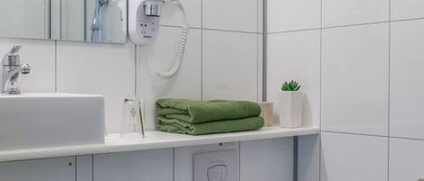 Une salle de bain moderne avec un lavabo blanc, des serviettes vertes, une petite plante en pot et des toilettes.