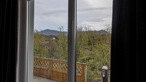 A view from a room with a large window overlooking a wooden deck and a mountainous landscape. - Vogahraun 4 (Myvatn)