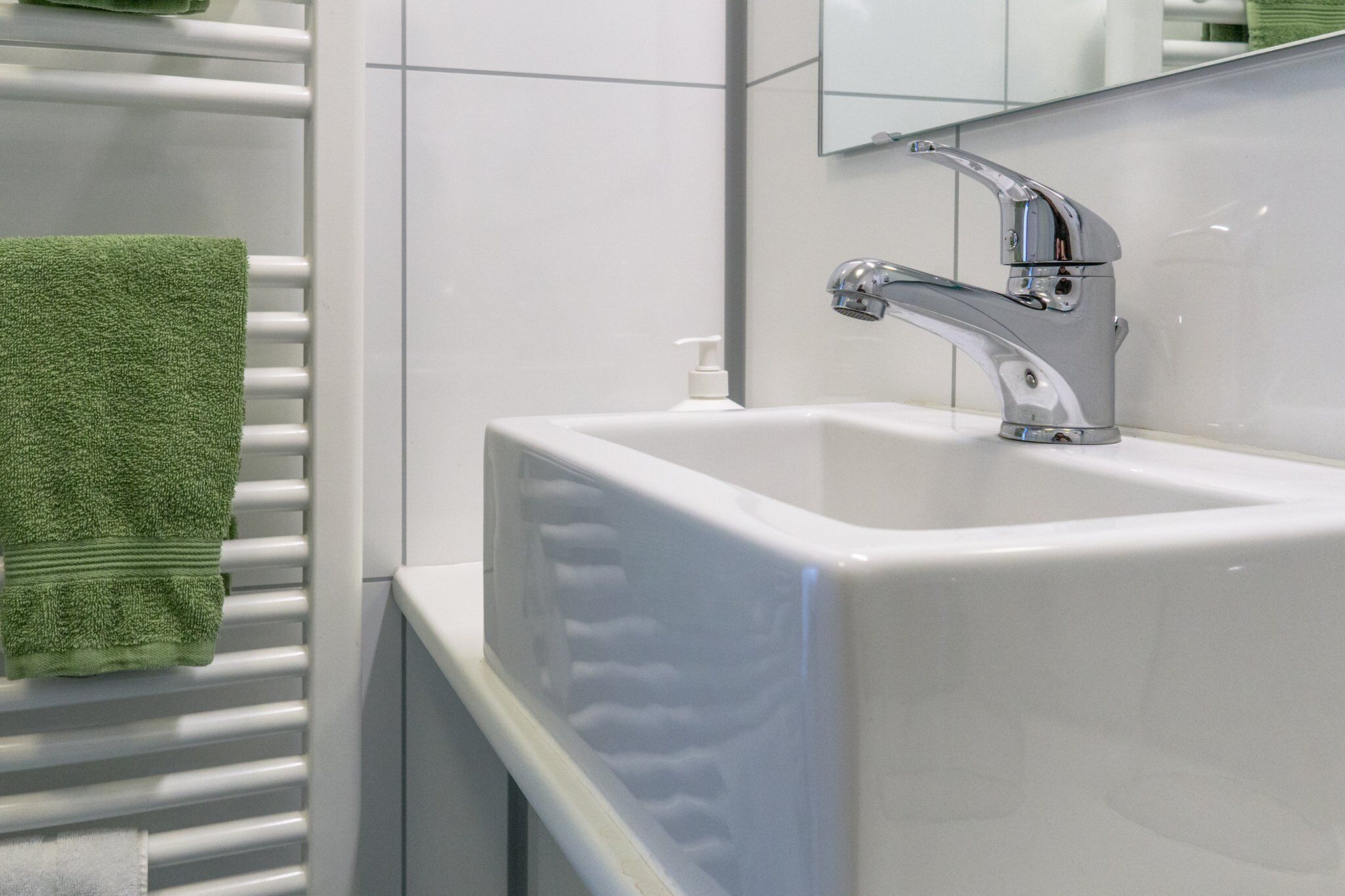 A white bathroom sink with a chrome faucet and a green towel on a white radiator.