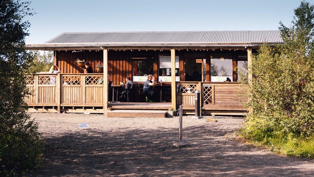 A wooden building with a covered patio area, outdoor seating, and a gravel ground. - Vogahraun 4 (Myvatn)
