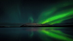 A night sky with visible stars and green aurora reflections on a calm water surface. - Vogahraun 4 (Myvatn)