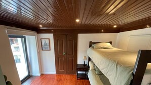 Een slaapkamer met een houten plafond, een bed, een groene stoel en een raam.
