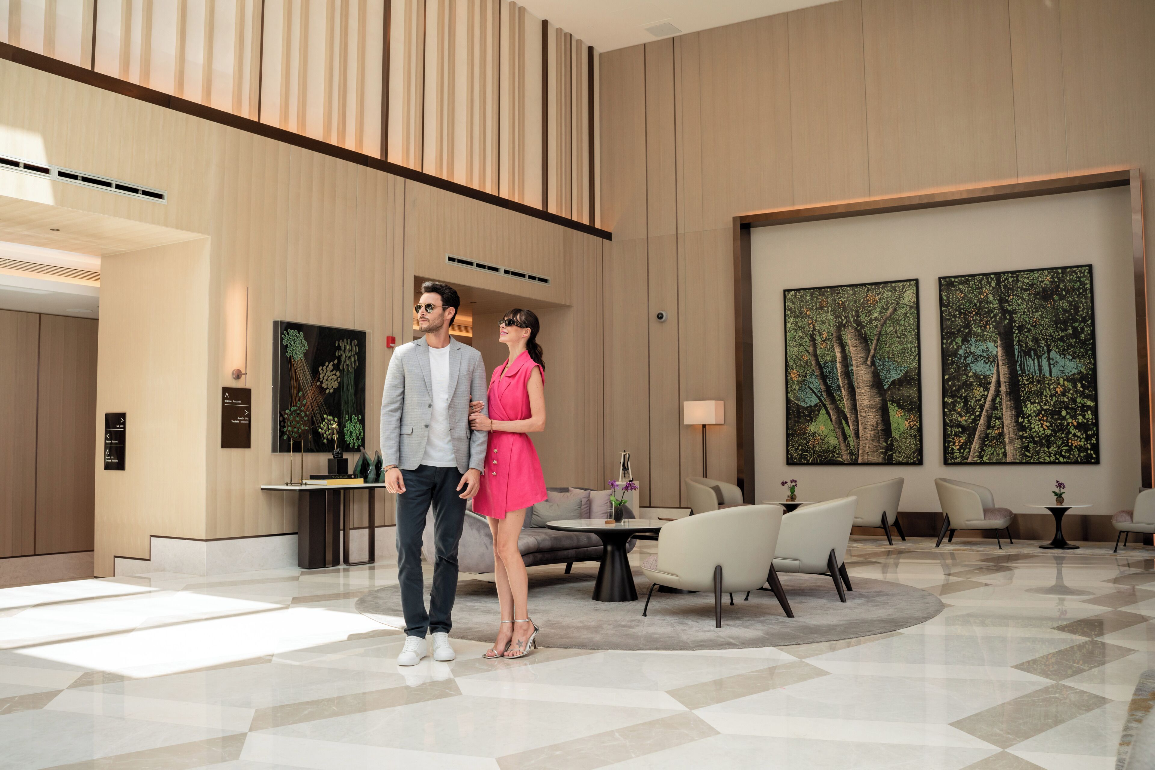 A modern hotel lobby with a high ceiling, a reception desk, seating area, and large windows with forest views.