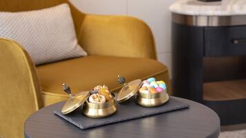 A small round table with two gold containers of chocolates and a bowl of colorful candies.