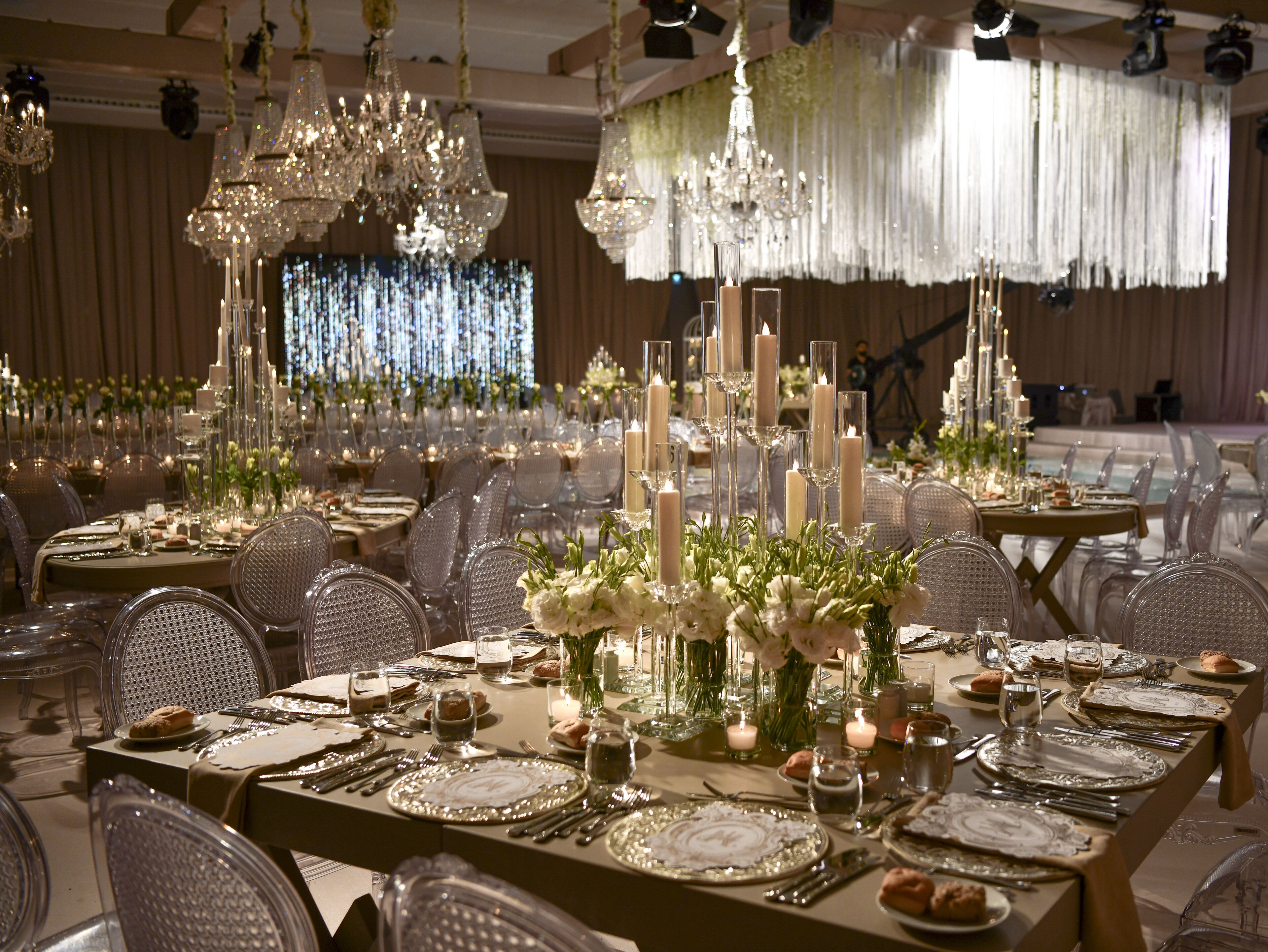 A banquet hall with tables set for a formal event, featuring crystal chandeliers, floral centerpieces, and candlelit tables.