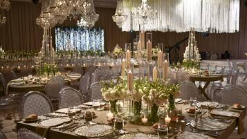 A banquet hall with tables set for a formal event, featuring crystal chandeliers, floral centerpieces, and candlelit tables.