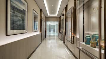 A modern hotel corridor with framed artwork on the walls, a polished floor, and glass-fronted display cases with decorative items.