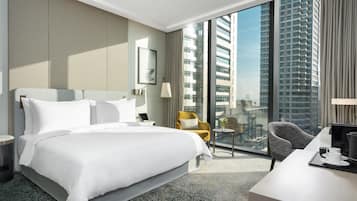 A hotel room with a large bed, a desk, a chair, and a view of tall buildings.