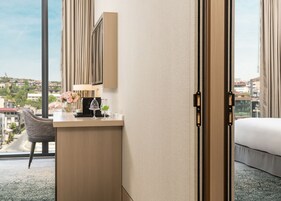 Habitación de hotel con cama, escritorio con lámpara, una silla y vista a la ciudad.