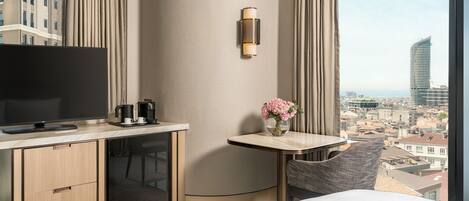 A hotel room with a bed, a desk with a TV, a coffee maker, and a vase with flowers.